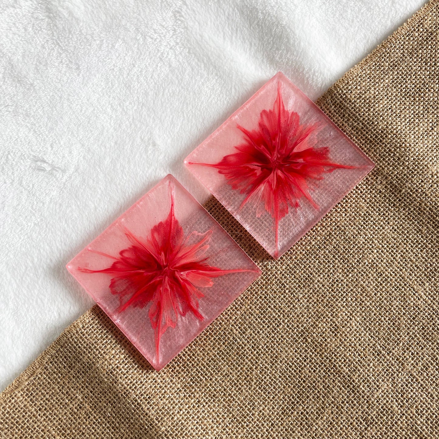 Square handmade resin drink coaster with pink and white marble effect shown on wooden table
